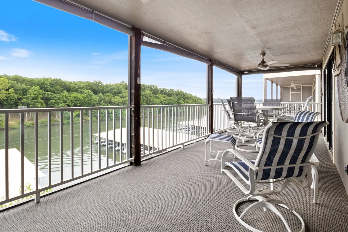 A tranquil balcony scene overlooking a river, equipped with comfortable outdoor seating and a sturdy railing. The setting is perfect for reading, sipping coffee, or socializing while taking in scenic views, especially during mornings or evenings.