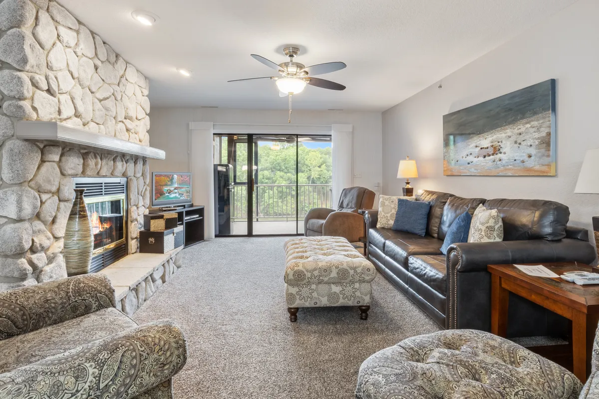 This inviting living area features a plush seating arrangement centered around a stone fireplace and accented by a large window with a scenic view. Decorative artwork and soft lighting contribute to a welcoming atmosphere, making it perfect for relaxing after a day at the lake or hosting a cozy movie night.