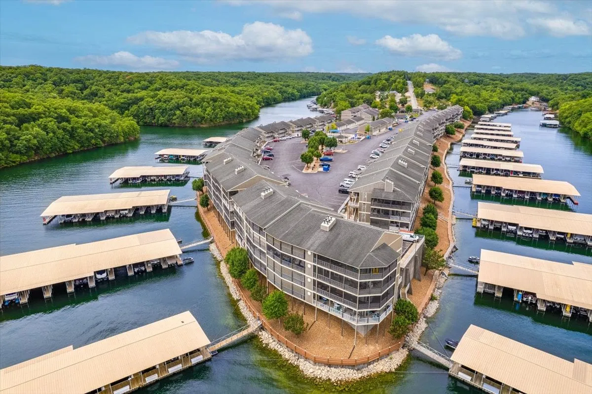 This vibrant lakefront scene captures the essence of Lake of the Ozarks, featuring the waterfront, a marina filled with boats, lush greenery, and the inviting architecture of the buildings. The water sparkles in the sunlight, promising endless opportunities for boating, fishing, and lakeside fun.
