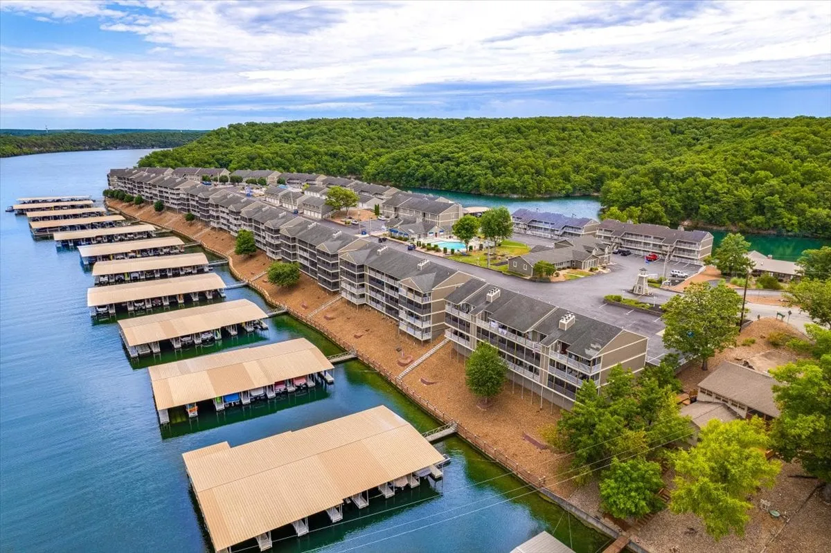 A scenic view of the lake framed by docks, buildings, and lush greenery, capturing the essence of Osage Beach as a hub for activities like boating, fishing, swimming, and picnicking. The vibrant waterfront setting offers hints of both leisurely and community-focused pursuits.