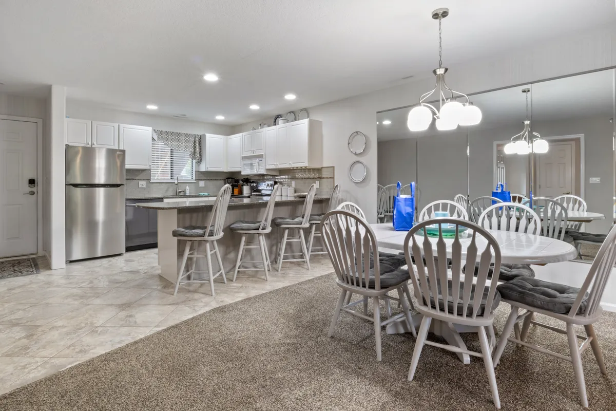 A bright dining area featuring a spacious table with ample seating, positioned adjacent to a modern kitchen with an island and stainless steel appliances. Stylish light fixtures overhead and open sightlines reinforce the feeling of a unified space, perfect for shared meals and conversations.