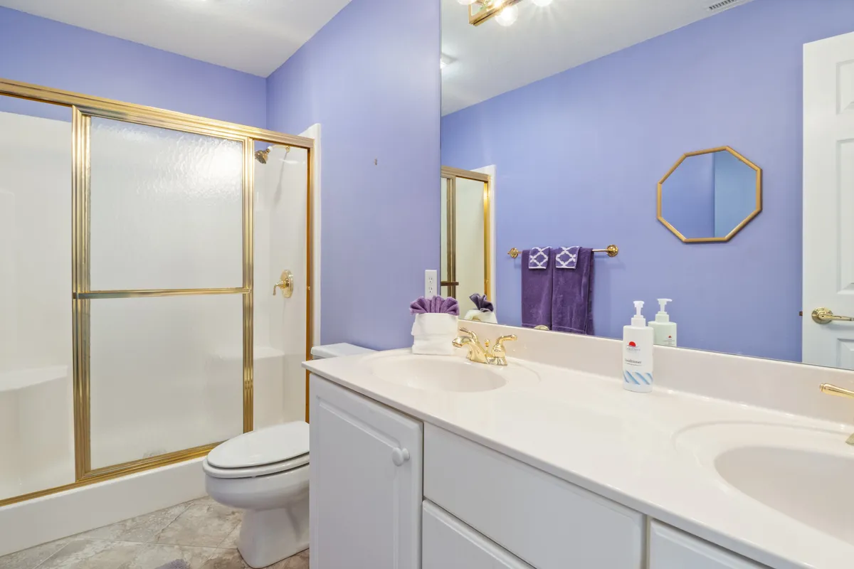 A modern bathroom with a vanity, shower enclosure, gold fixtures, and a large mirror. The space is well-lit and designed for comfort, offering a refreshing and serene atmosphere for morning or evening routines.